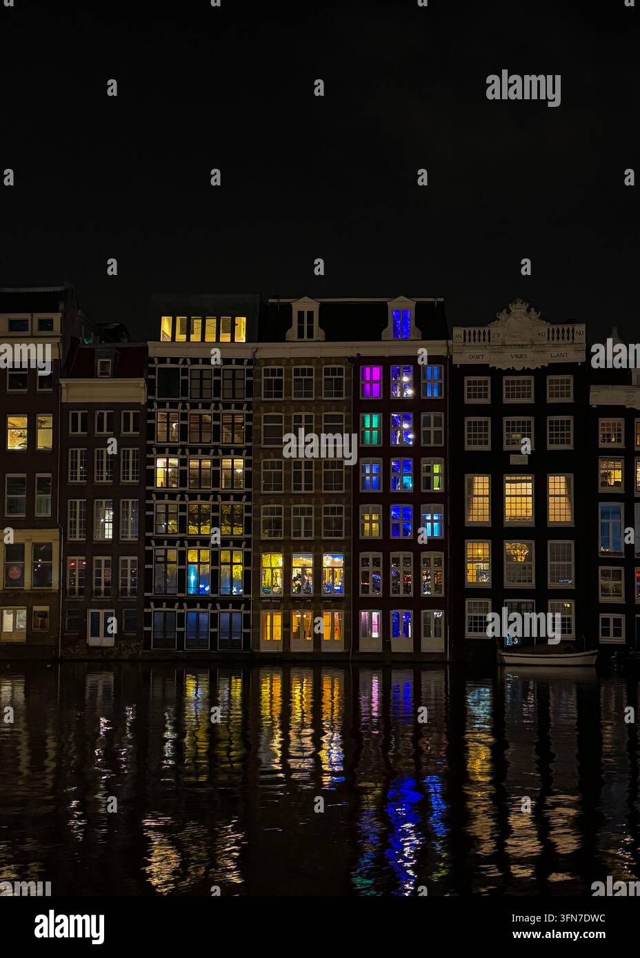 Maisons des canaux d'Amsterdam avec des fenêtres illuminées colorées reflétées dans le canal la nuit, Pays-Bas. - Image de stock capturée avec un smartphone