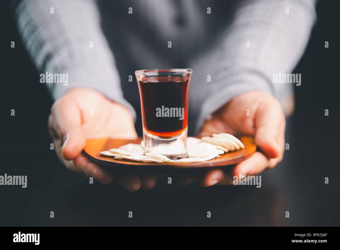 Personne offrant une assiette en bois de hosties et une boisson rouge foncé vers le spectateur, illustrant la communion chrétienne, le culte, le partage sacré Banque D'Images
