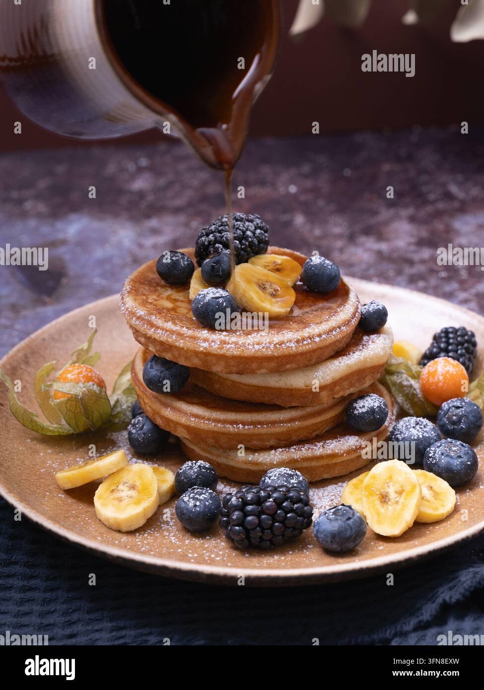 Du sirop d'érable est versé sur une pile de crêpes maison garnies de figues fraîches, de myrtilles, de mûres et de baies dorées Banque D'Images