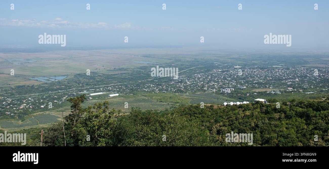 Panorama élevé montrant des sighnaghi répandus dans la vallée, avec des collines boisées au premier plan, des champs cultivés, des bâtiments dispersés et des montagnes brumeuses b Banque D'Images