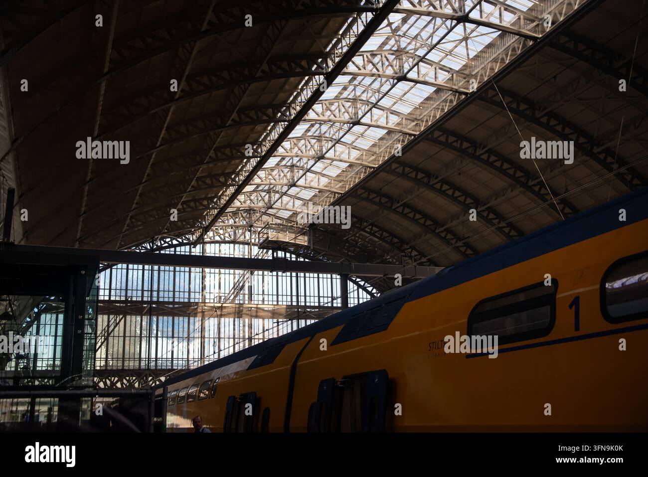 15 juillet 2024 - Amsterdam, Pays-Bas : Un train passager à étages jaunes se tient sous les poutres en acier et le toit en verre d'Amsterdam Centraal s Banque D'Images