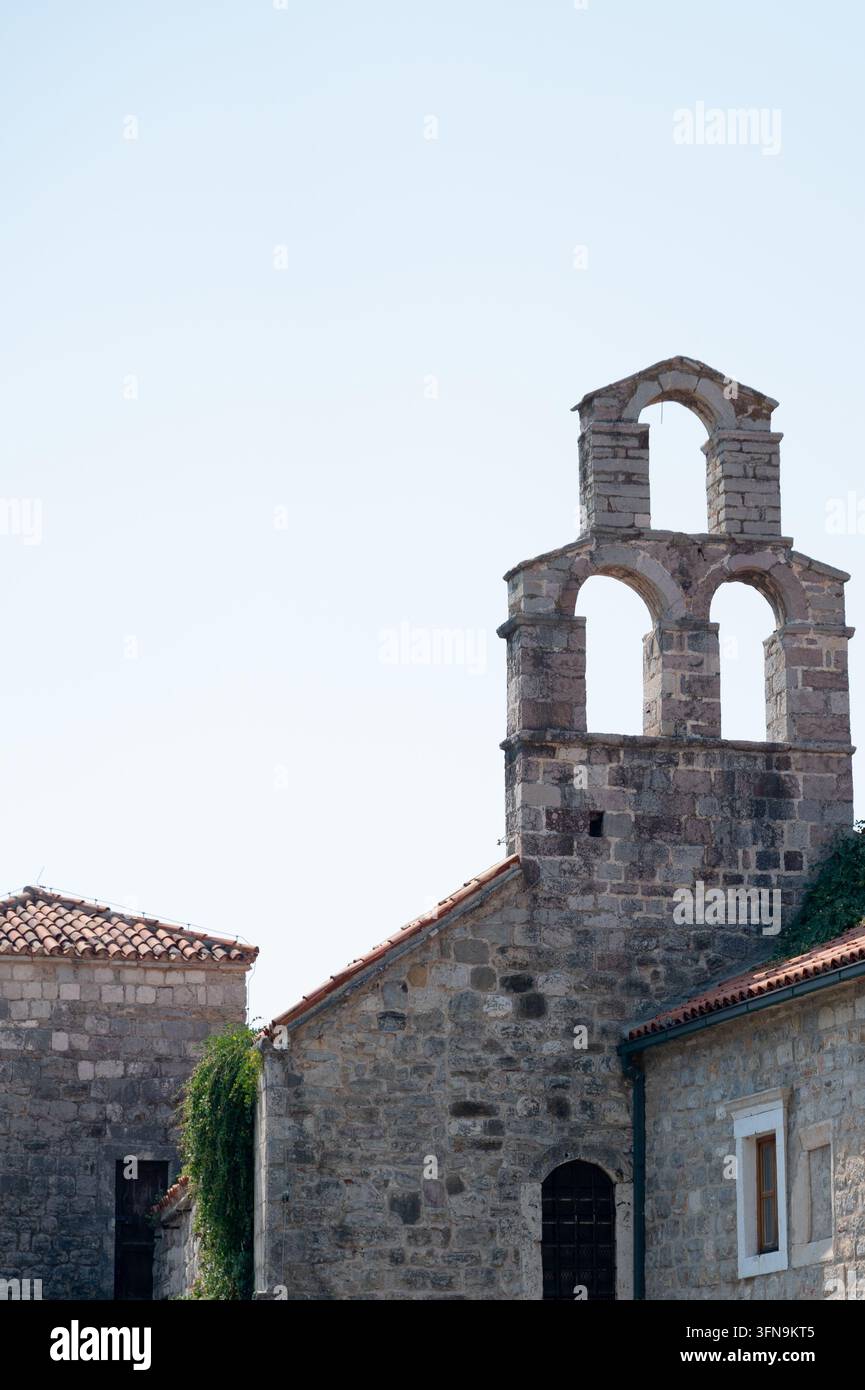 Petite chapelle en pierre avec clocher et ouvertures en arc sous un ciel clair et pâle, toits carrelés et lierre grimpant sur la maçonnerie érodée pour le voyage et le patrimoine Banque D'Images