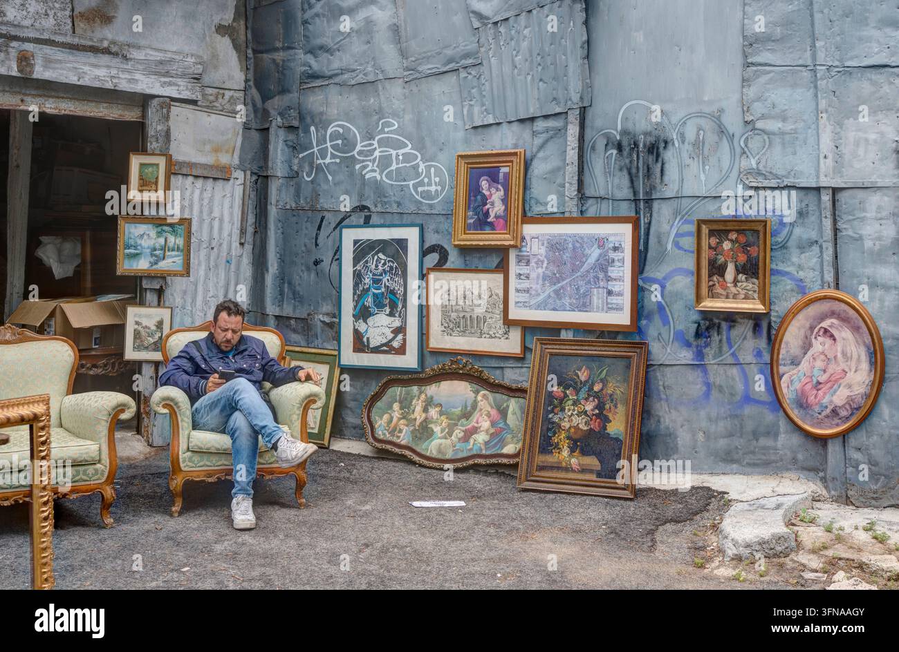 Marchand d'antiquités senior assis devant des peintures d'art classique dans une boutique d'antiquités à Palerme, Sicile, Italie. Style de vie local authentique Banque D'Images