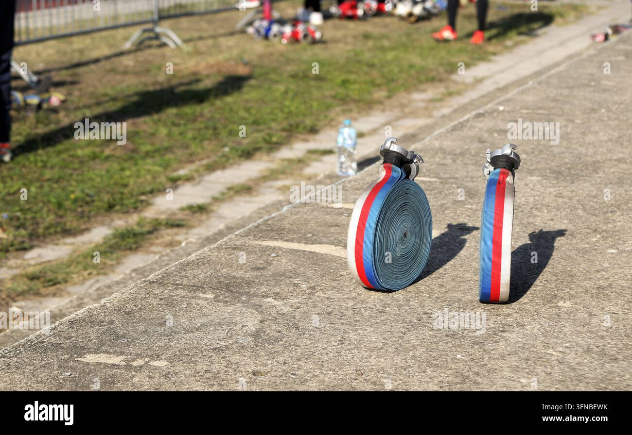 Les tuyaux d'incendie, colorés rouge, blanc et bleu, sont soigneusement enroulés et reposent sur une surface en béton, prêts pour une compétition de sports nautiques en plein air sur Banque D'Images