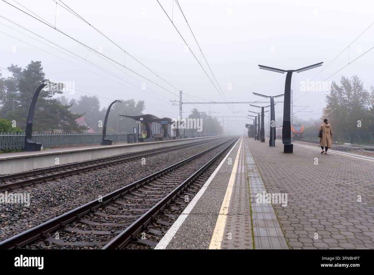 Tallinn, Estonie – 2 octobre 2026 : Voies ferrées, quais et câbles aériens à la gare de Paaskula dans le brouillard, avec une personne sur le quai. Banque D'Images