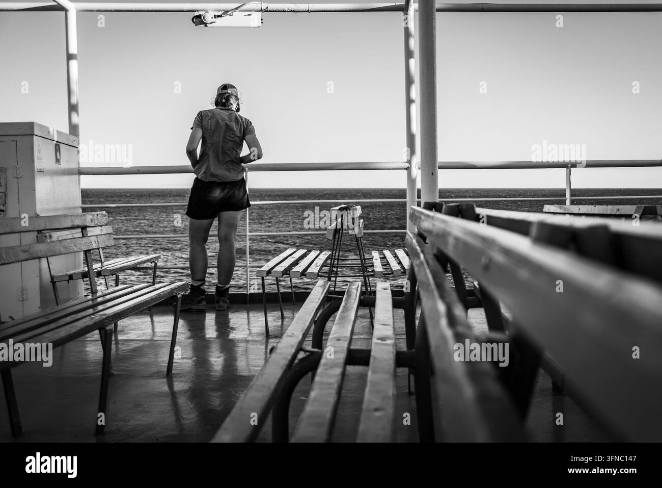 Vue arrière d'une jeune touriste appuyée sur la rambarde d'un pont de ferry avec des bancs en bois, contemplant la mer Méditerranée bleue et ouverte, Grèce Banque D'Images