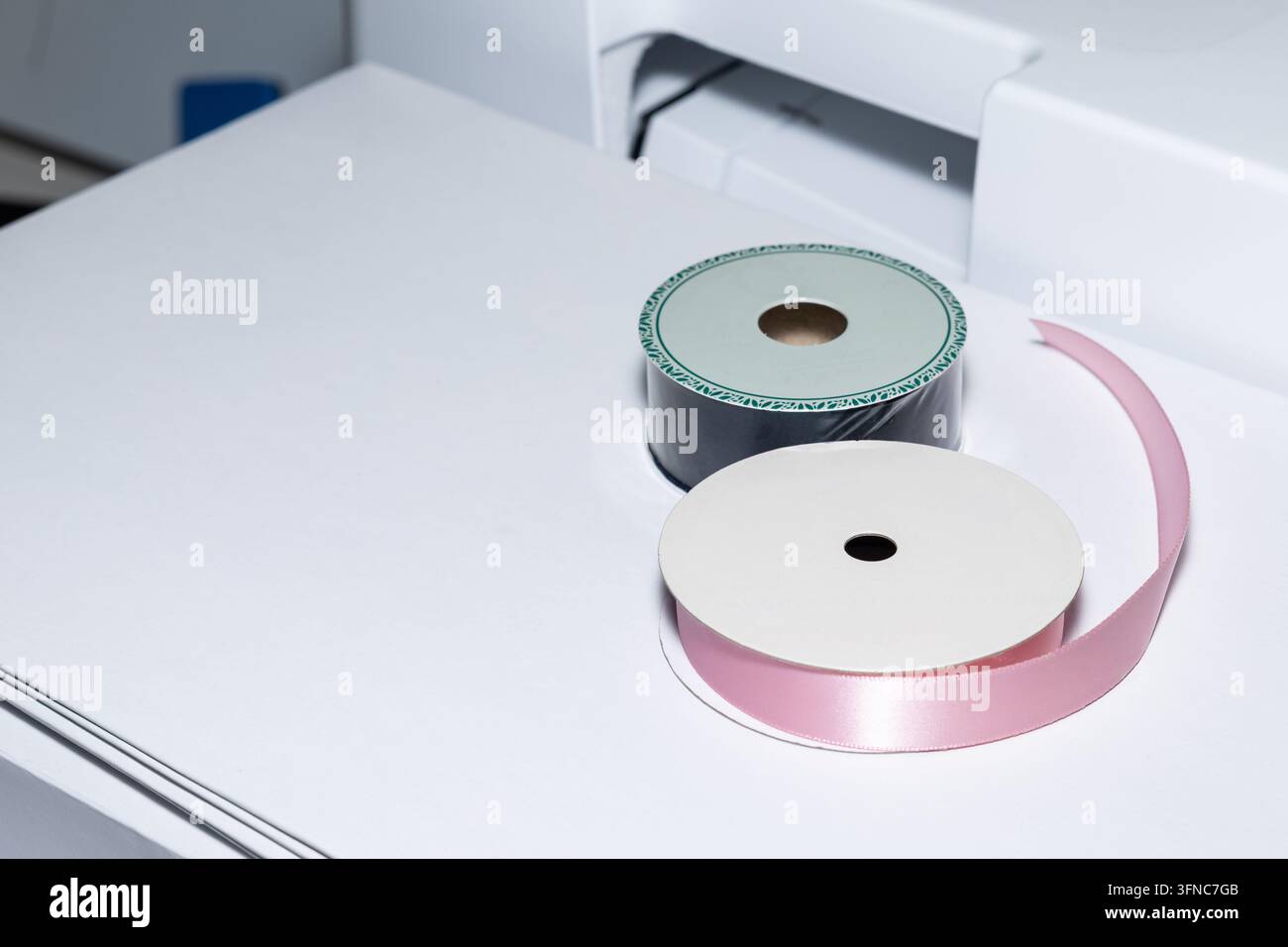 Ruban de satin rose et bobines de ruban sombre sur du papier blanc à côté de la machine à coudre, créant un artisanat propre Banque D'Images