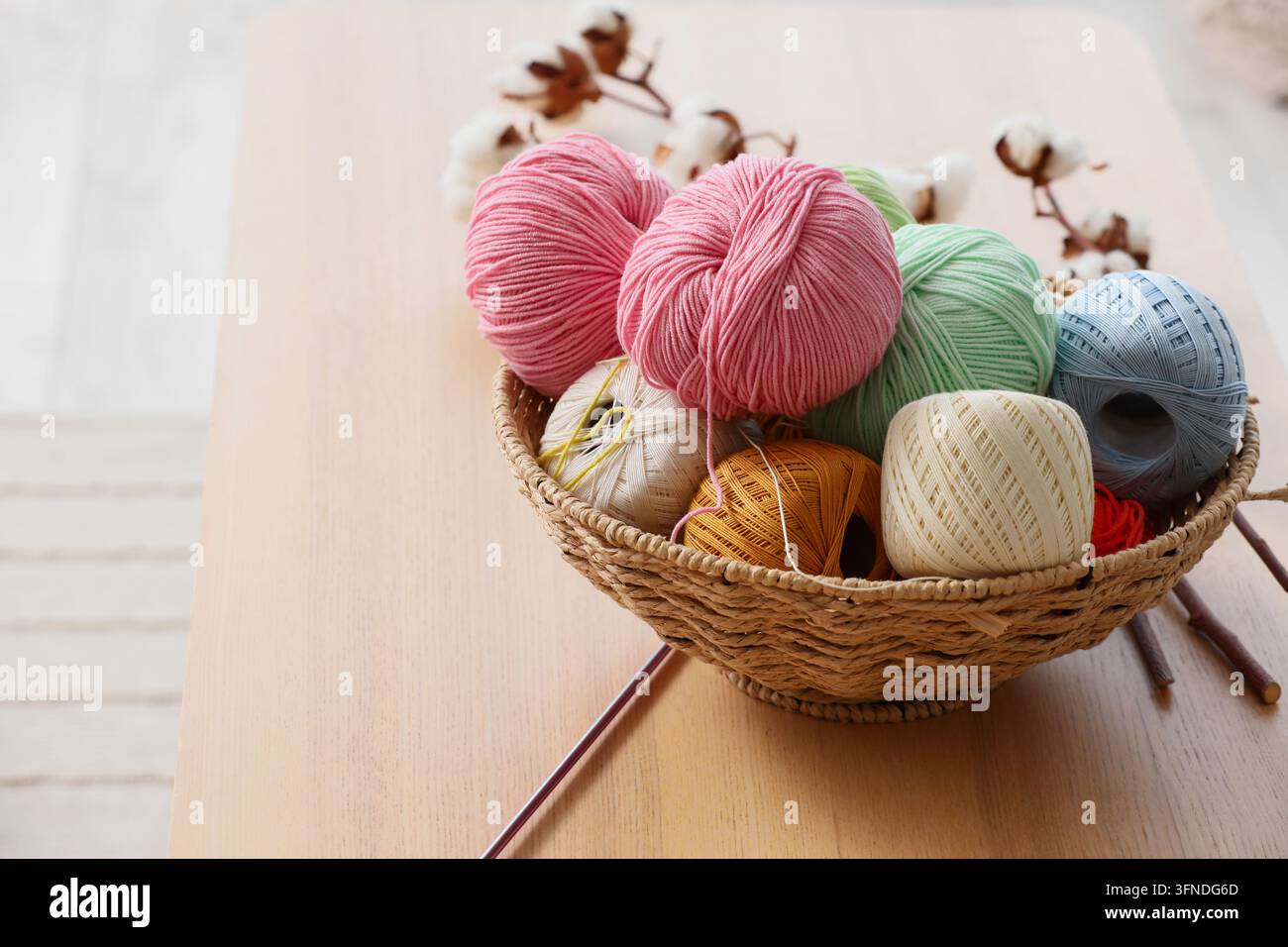 Artisanat et loisirs créatifs, boules de laine colorées dans un panier en osier avec des fleurs en coton pour des projets de tricot et de crochet sur une surface de table en bois Banque D'Images
