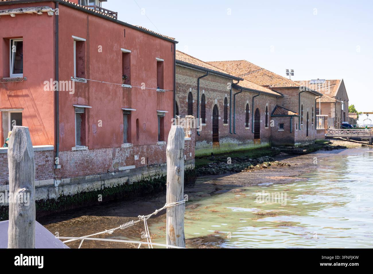 Des bâtiments en stuc coloré et en briques apparentes bordent un canal de Venise, avec des tuiles de toit en terre cuite, des fenêtres, des tuyaux de drainage, des poteaux d'amarrage en bois, des cordes, et Banque D'Images