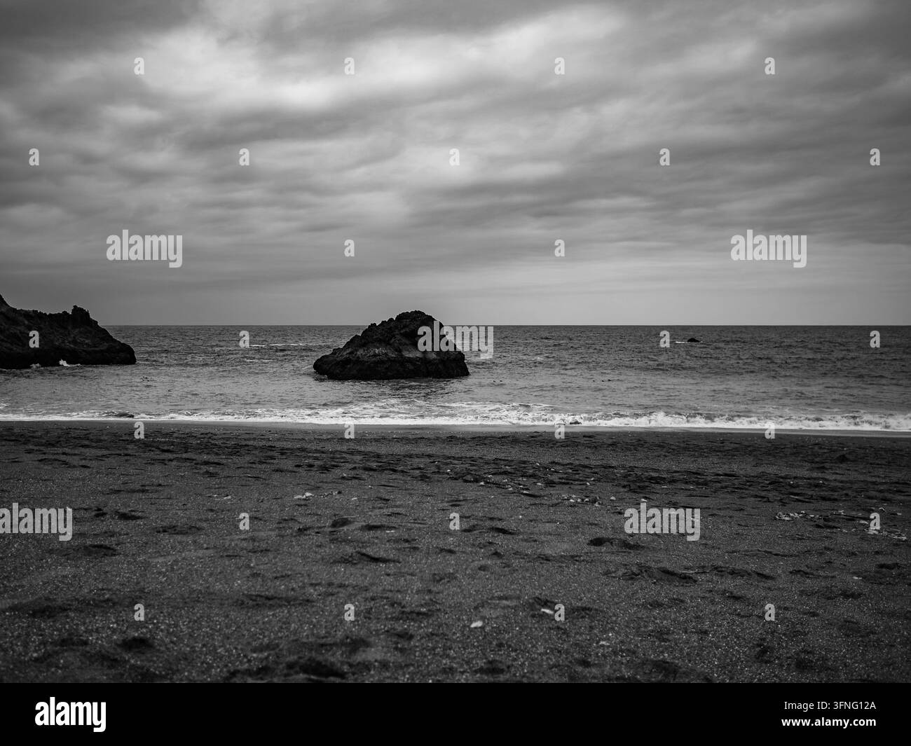 De gros nuages couverts planent sur une plage de sable sombre avec des falaises maritimes au large Banque D'Images