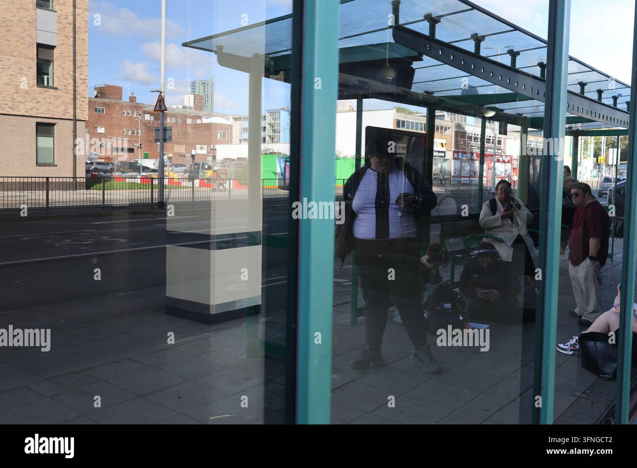 Passagers attendant à l'intérieur d'un abribus moderne en verre dans un carrefour de transport urbain. Banque D'Images