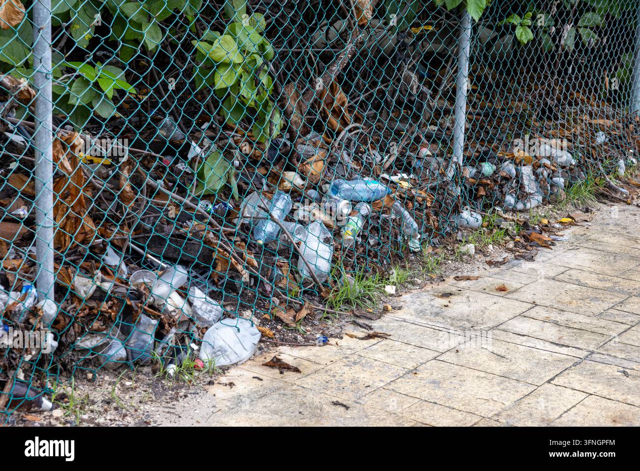 Bouteilles en plastique et déchets empilés contre une clôture en grillage sur un trottoir urbain – Problème de pollution environnementale Banque D'Images