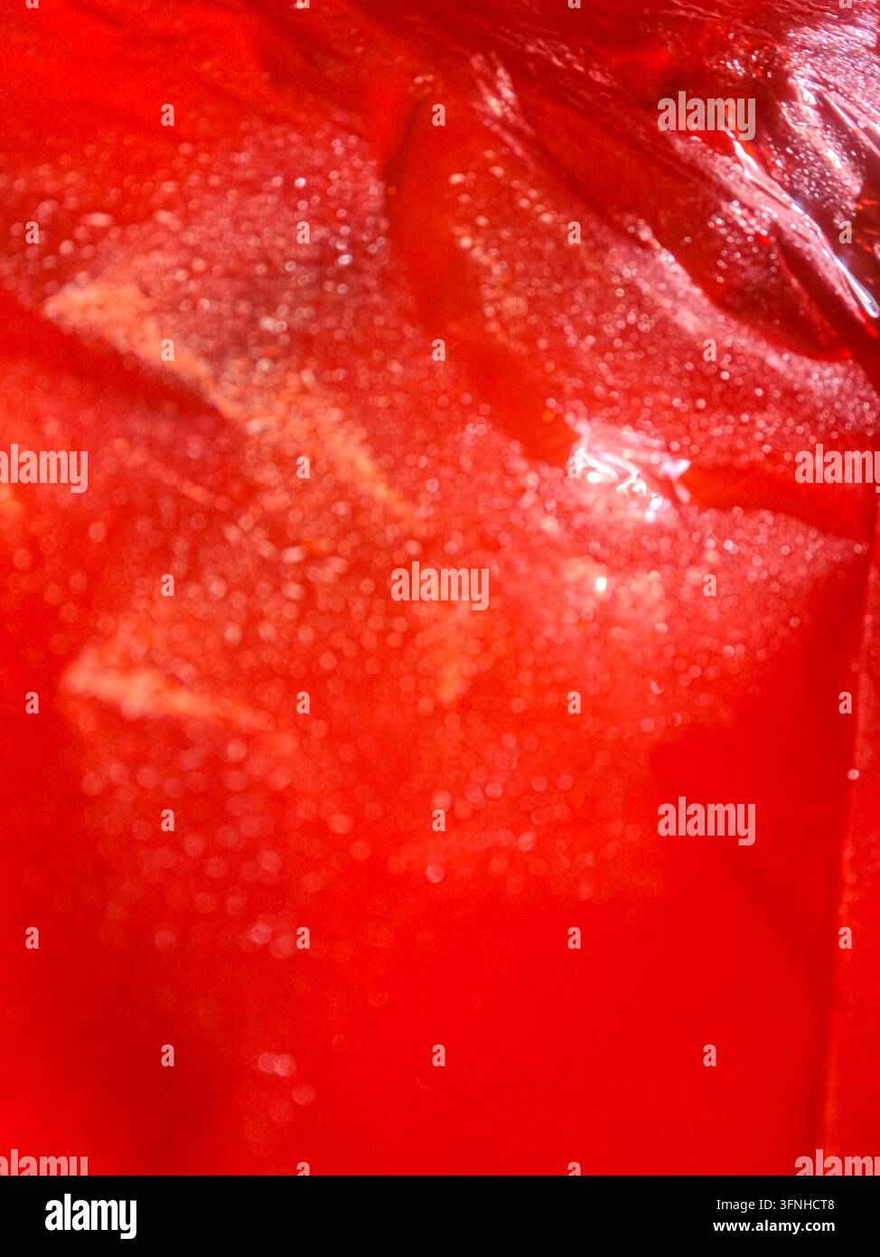 Vue abstraite en gros plan d'un liquide rouge avec des glaçons. Les bulles et la condensation créent une texture. Couleurs vives et éclatantes adaptées aux rafraîchissements et aux célébrations Banque D'Images