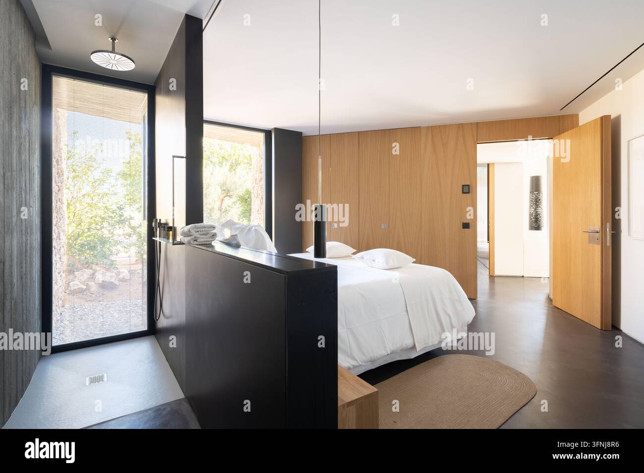 Une chambre lumineuse et contemporaine dans une villa de luxe en Catalogne, Espagne, dotée d'une douche noire, d'un lit blanc, de lambris en bois, de grandes fenêtres et d'un design épuré Banque D'Images