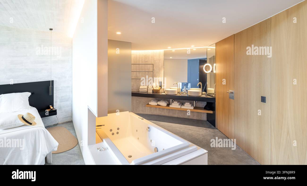 Salle de bain élégante dans une villa de luxe en Catalogne, dotée d'une baignoire spa, d'une double vasque, de lambris en bois, d'un éclairage doux et d'un aperçu d'une chambre moderne Banque D'Images