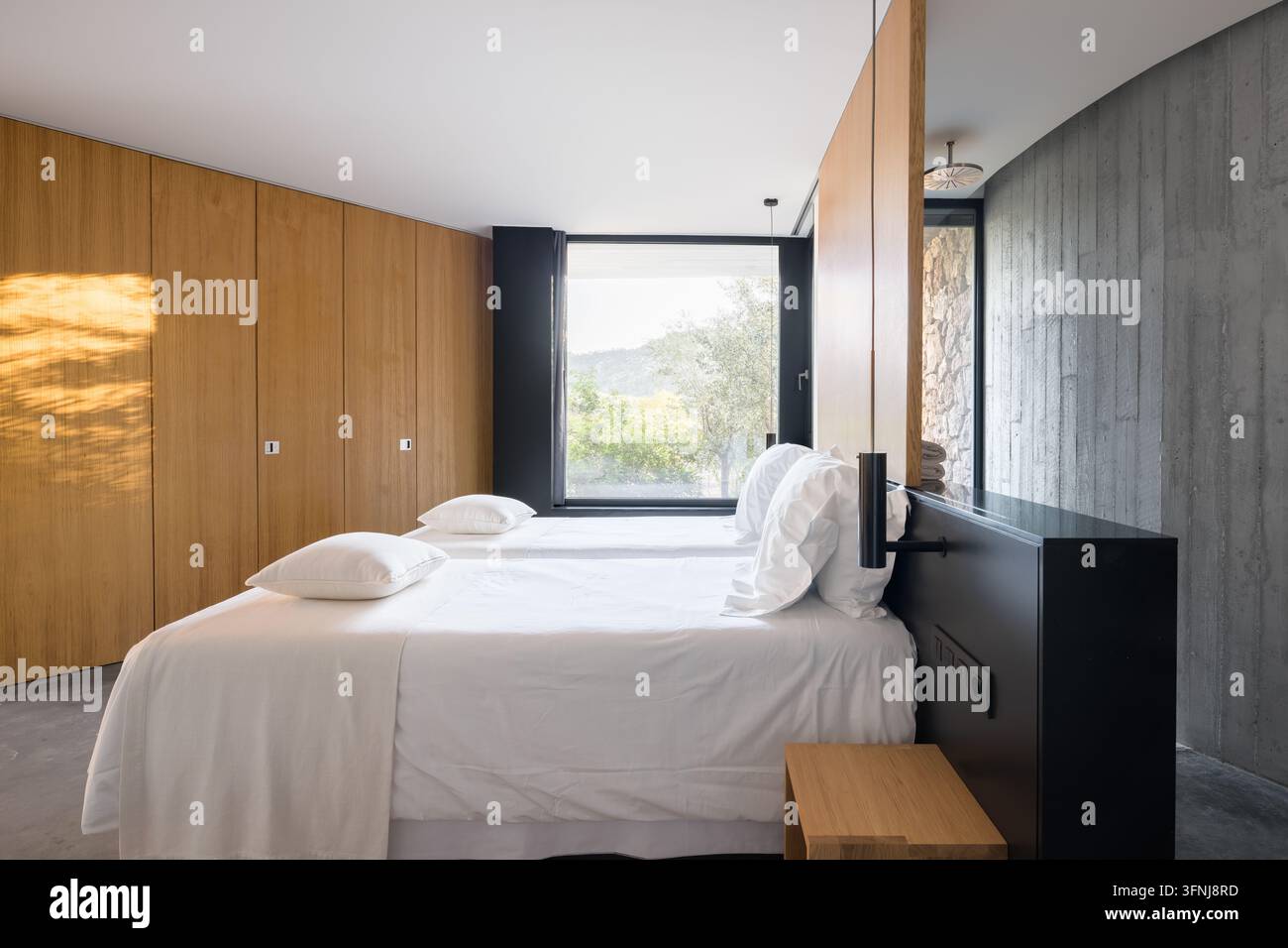 Chambre élégante dans une villa de luxe en Catalogne, dotée d'un lit double blanc, de lambris en bois chaud, d'un mur d'accent sombre, d'une grande fenêtre et d'un min contemporain Banque D'Images