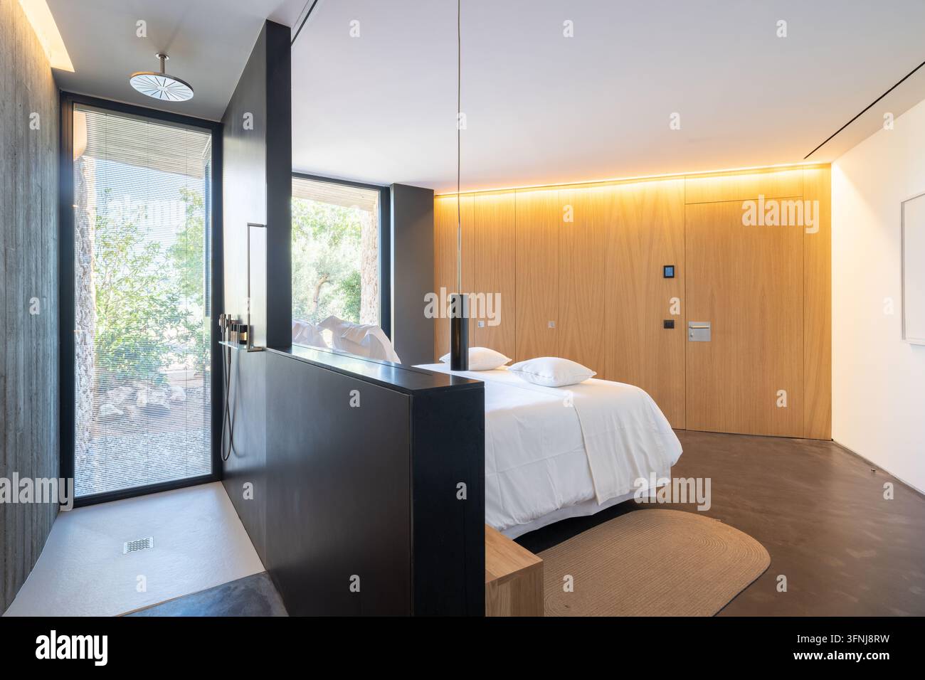 Une chambre lumineuse et contemporaine dans une villa de luxe en Catalogne, Espagne, dotée d'une douche noire, d'un lit blanc, de lambris en bois, de grandes fenêtres et d'un design épuré Banque D'Images