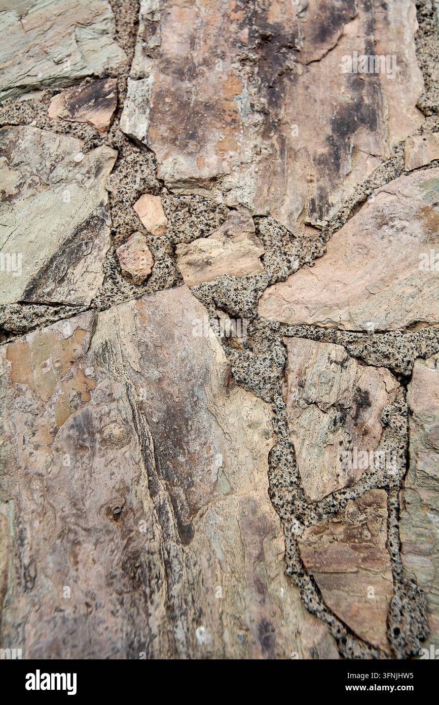 Image de fond verticale d'un mur en pierre naturelle rustique présentant des dalles d'ardoise multicolores jointes avec un mortier sablonneux. Banque D'Images