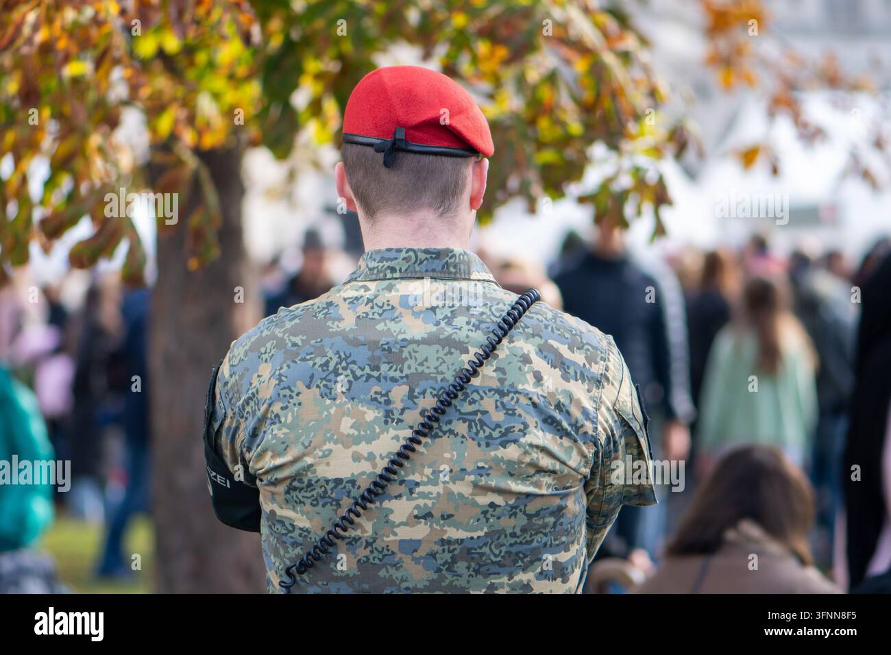 VIENNE, AUTRICHE, 26 octobre 2025 : Un soldat en uniforme de camouflage et béret rouge se tient debout avec une foule floue à l'extérieur. Banque D'Images