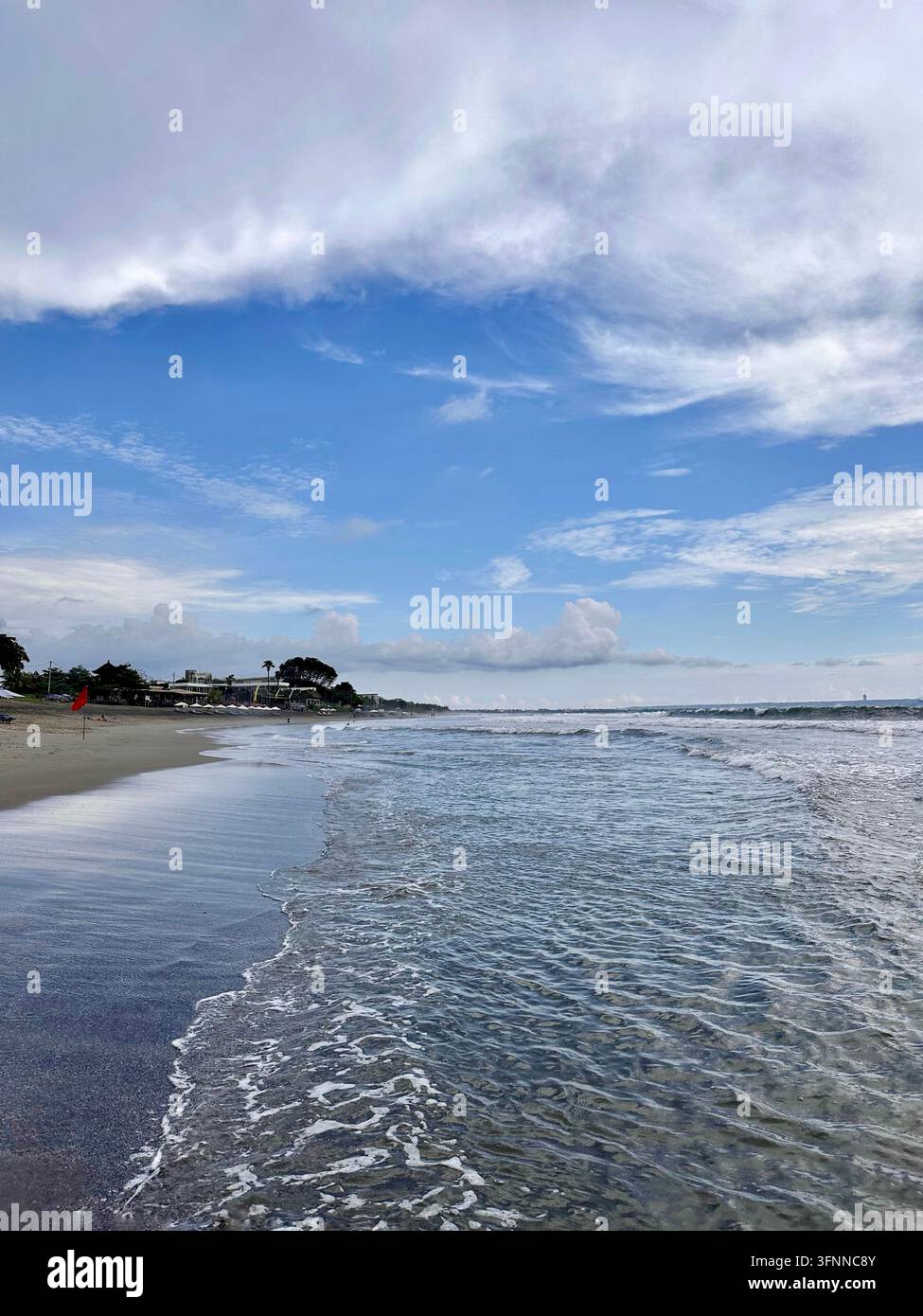 Des vagues d'océan moussantes lavent une côte sablonneuse sous un ciel bleu et des nuages en couches. - Image de stock capturée avec un smartphone