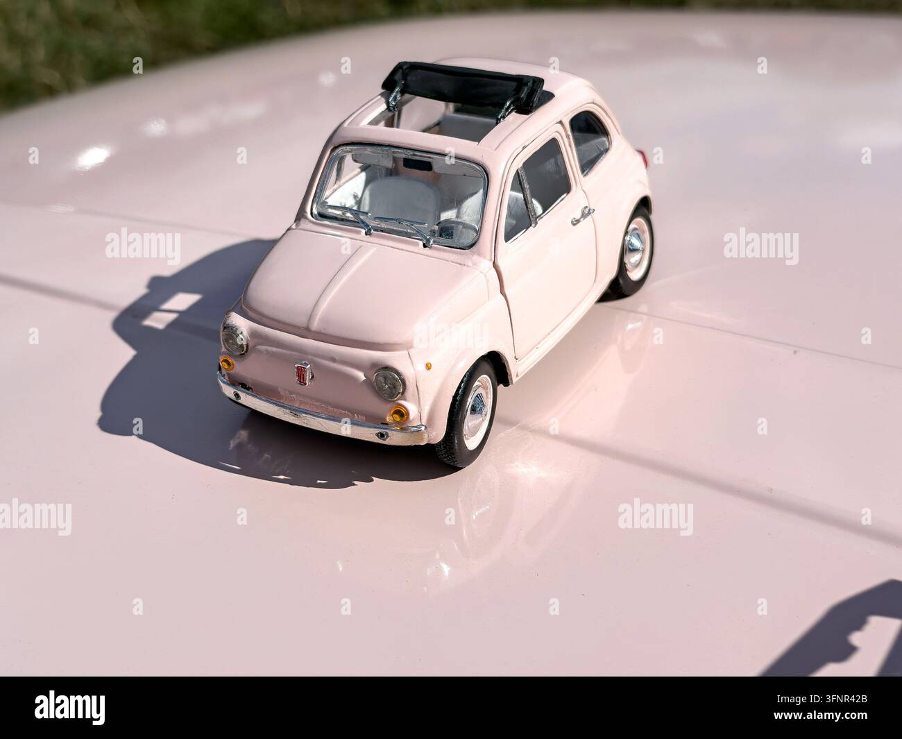 réplique de jouet en métal classique Fiat 500 rose reposant sur le capot rose d'une voiture vintage Fiat Cinquecento grandeur nature - Image de stock capturée avec un smartphone