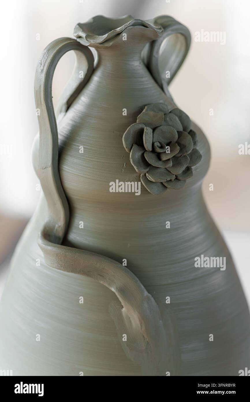 Vase en poterie non émaillée faite à la main, avec des poignées décoratives, un bord ondulé, une rose en argile détaillée et des éléments en relief courbés, mettant en valeur l'artisanat Banque D'Images