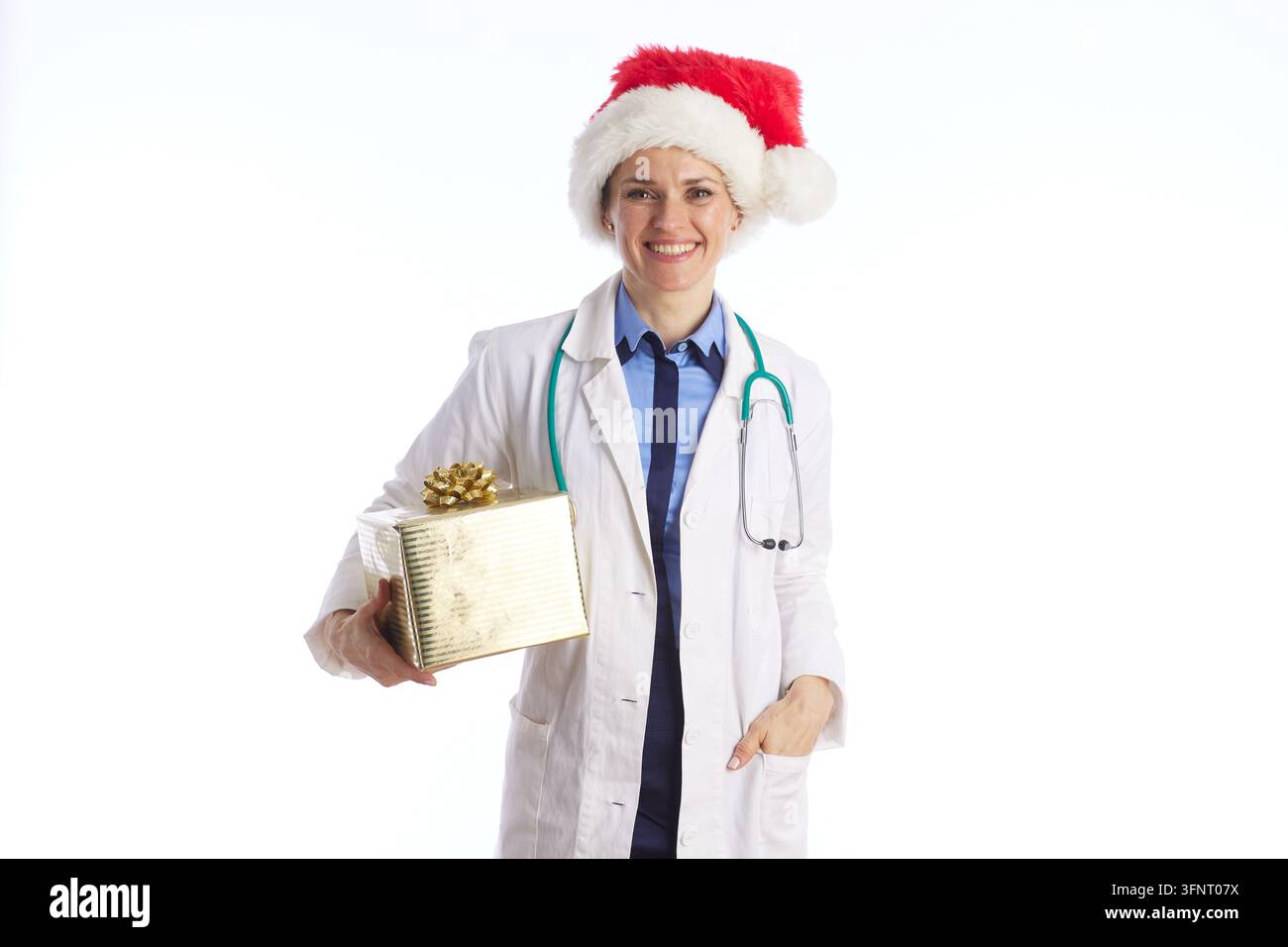Une médecin porte un chapeau de Père Noël et tient une boîte cadeau en or, représentant le professionnalisme médical mêlé à la chaleur des fêtes et au bien-être saisonnier. Banque D'Images