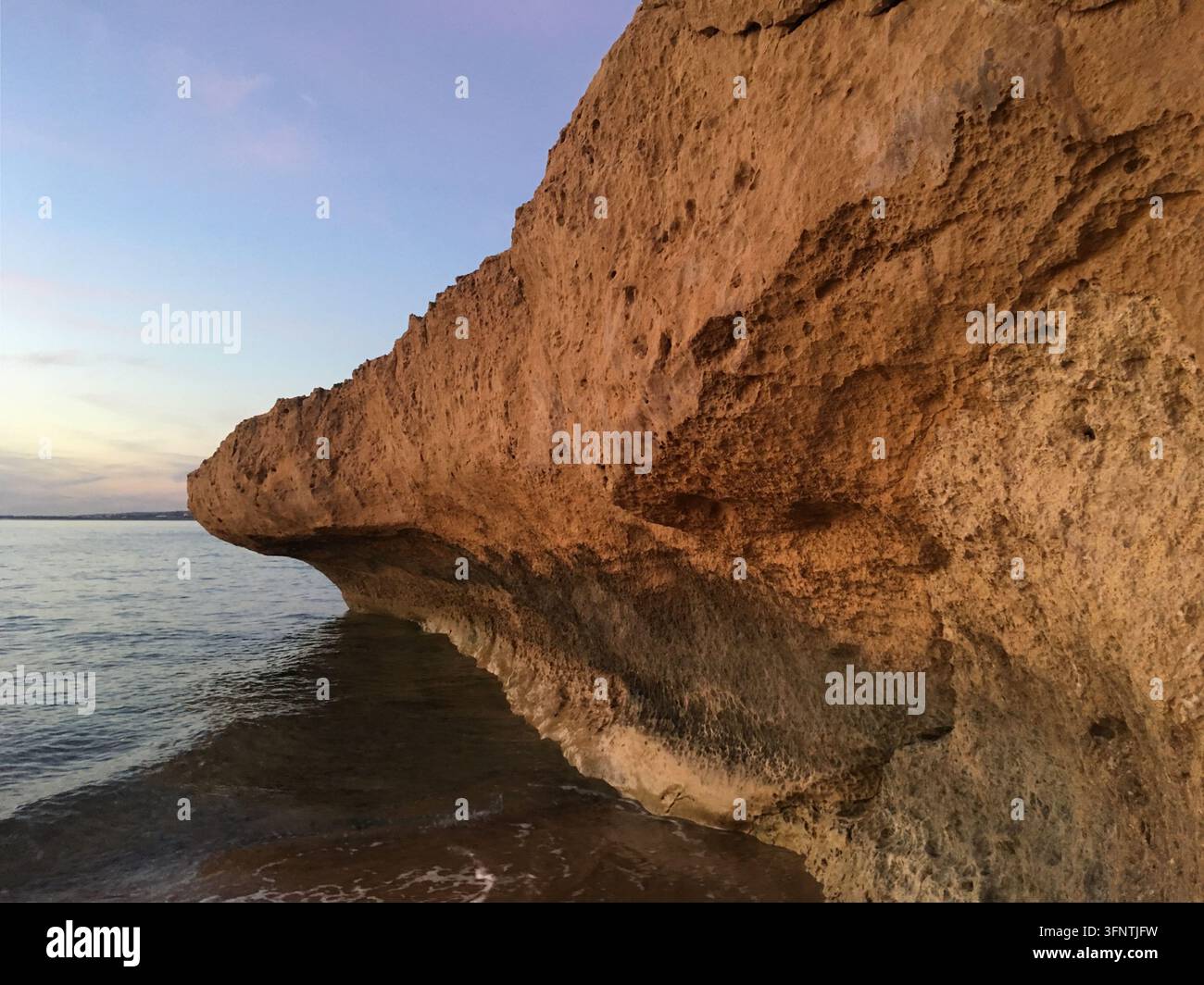 Formation rocheuse côtière à Paphos, Chypre, présentant des textures abruptes et un surplomb proéminent. Les tons chauds et terreux de la roche contrastent avec le calme du bl Banque D'Images