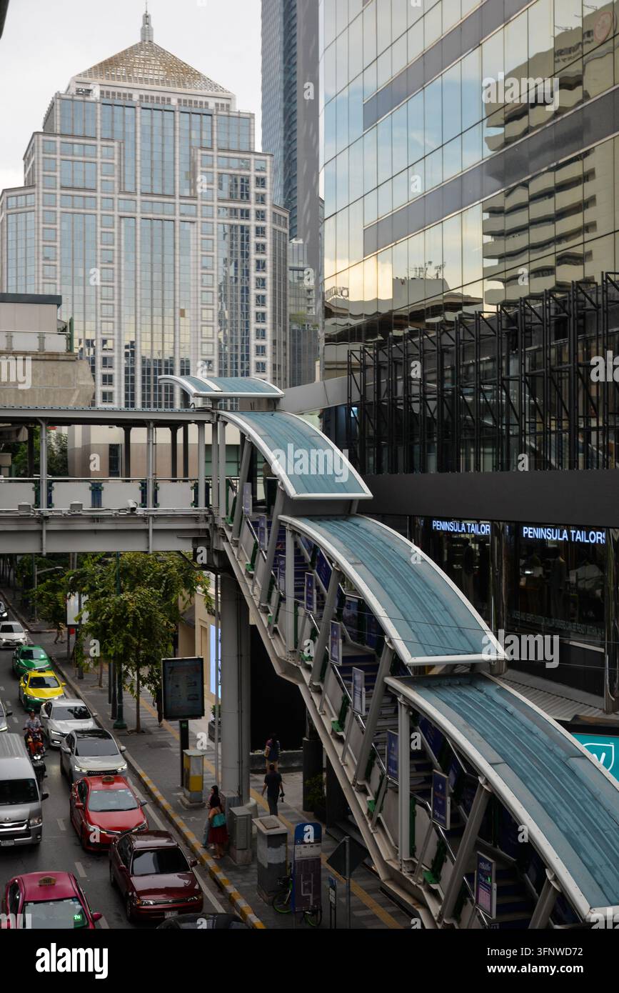 BANGKOK, THAÏLANDE – 5 JUILLET 2026 : Passerelle piétonne surélevée et bâtiments commerciaux modernes dans le quartier Ratchaprasong de Bangkok, avec des taxis colorés Banque D'Images