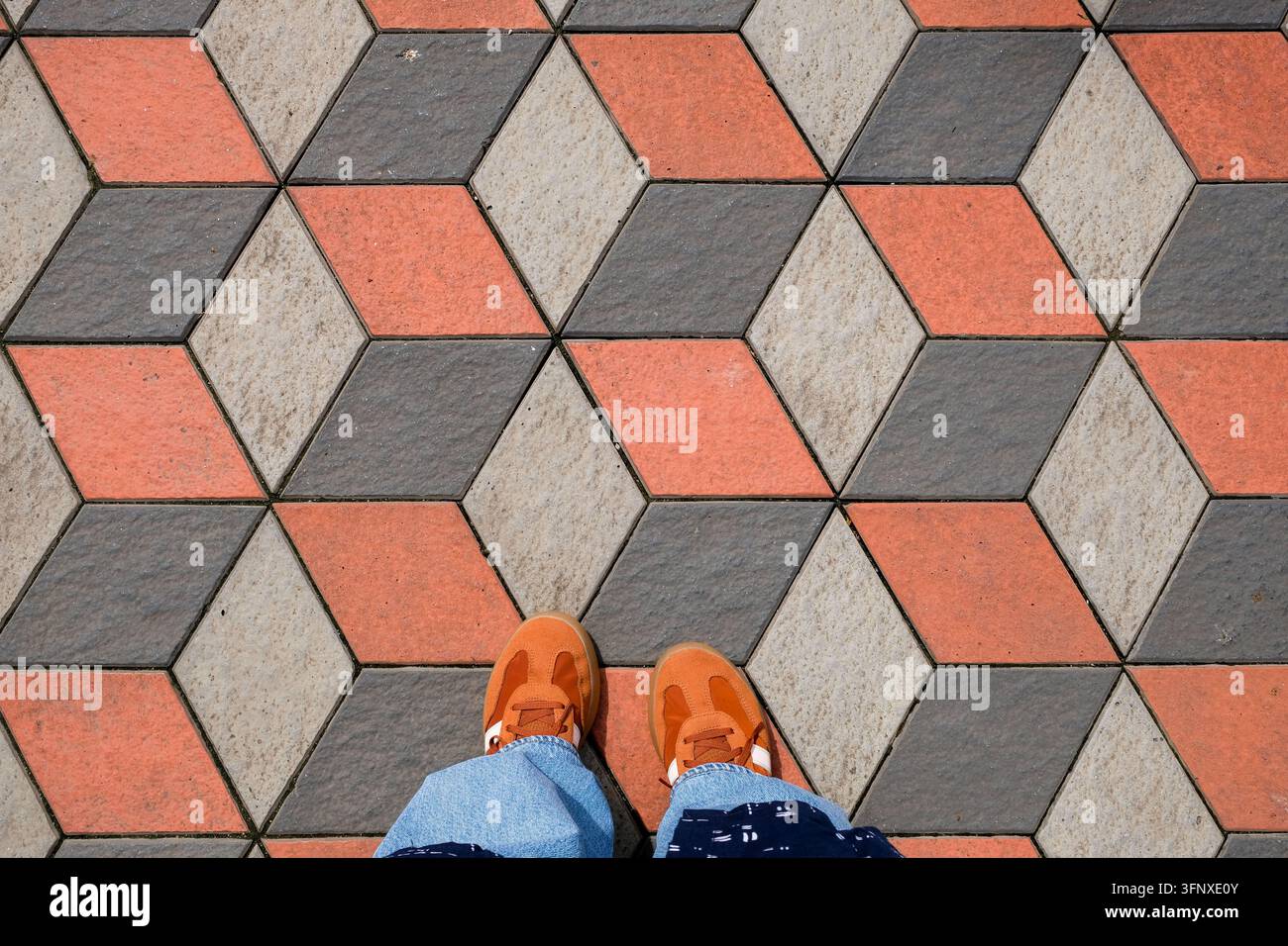 Gombak, Malaisie – 18 mai 2026 : Baskets orange vives sur un pavé d’illusion optique géométrique en 3D Banque D'Images