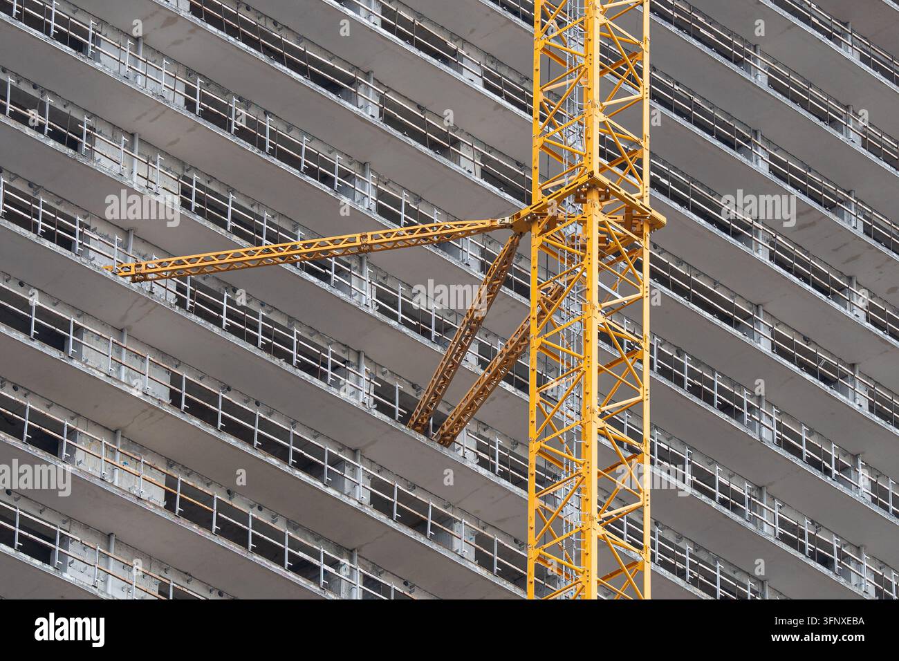 Une attache d'ancrage lourde relie la grue tournante aux dalles de sol d'un bâtiment moderne en construction. Banque D'Images