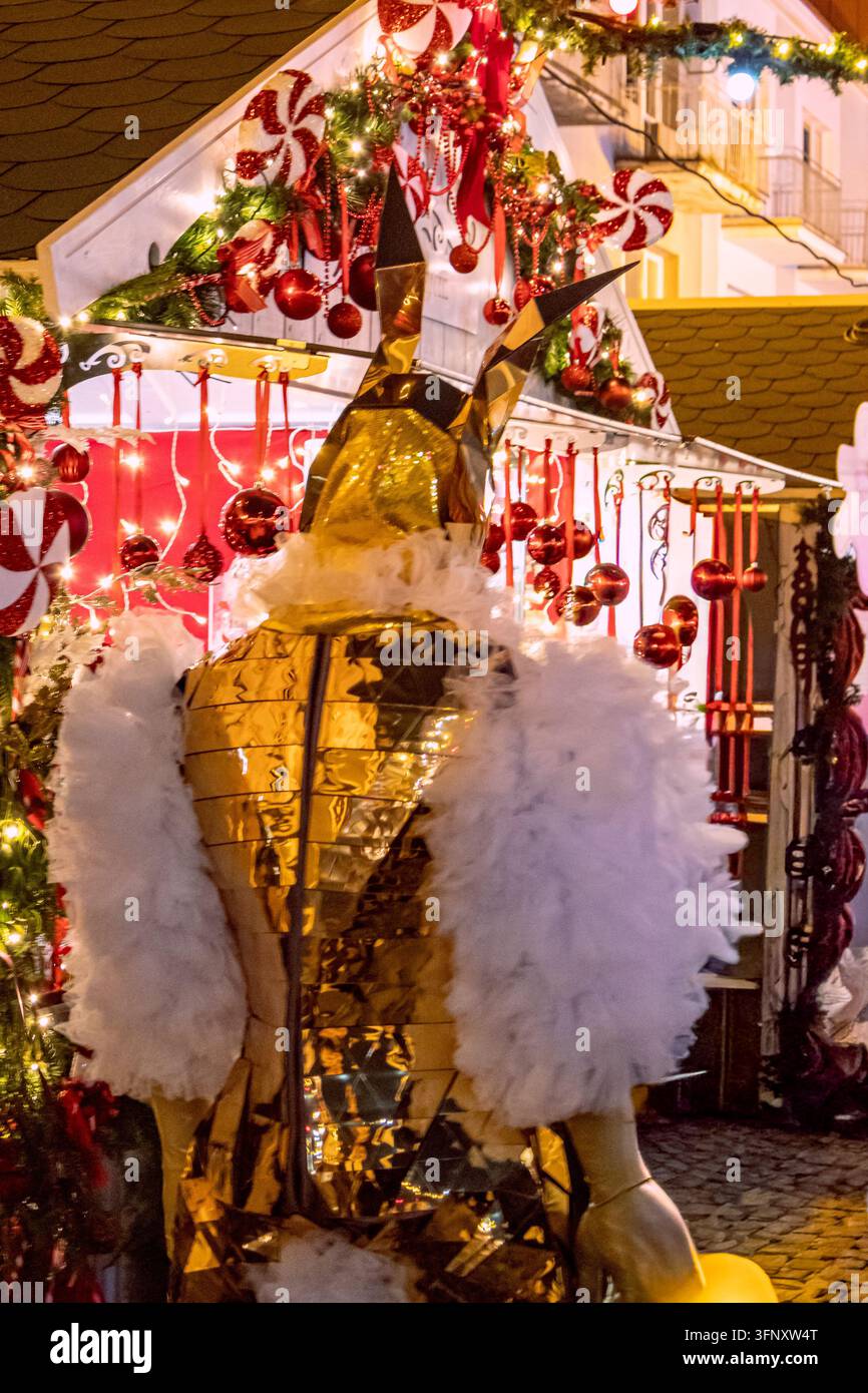 Bialystok, Pologne – 4 décembre 2025 : Artiste vêtu d’un costume de lapin miroir doré se tient devant des étals de marché de Noël décorés avec des ornements de bonbons Banque D'Images