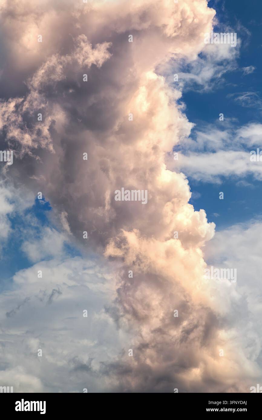 Un nuage cumulus imposant s'élève contre un ciel bleu vif, illuminé par les tons chauds du coucher de soleil. Banque D'Images