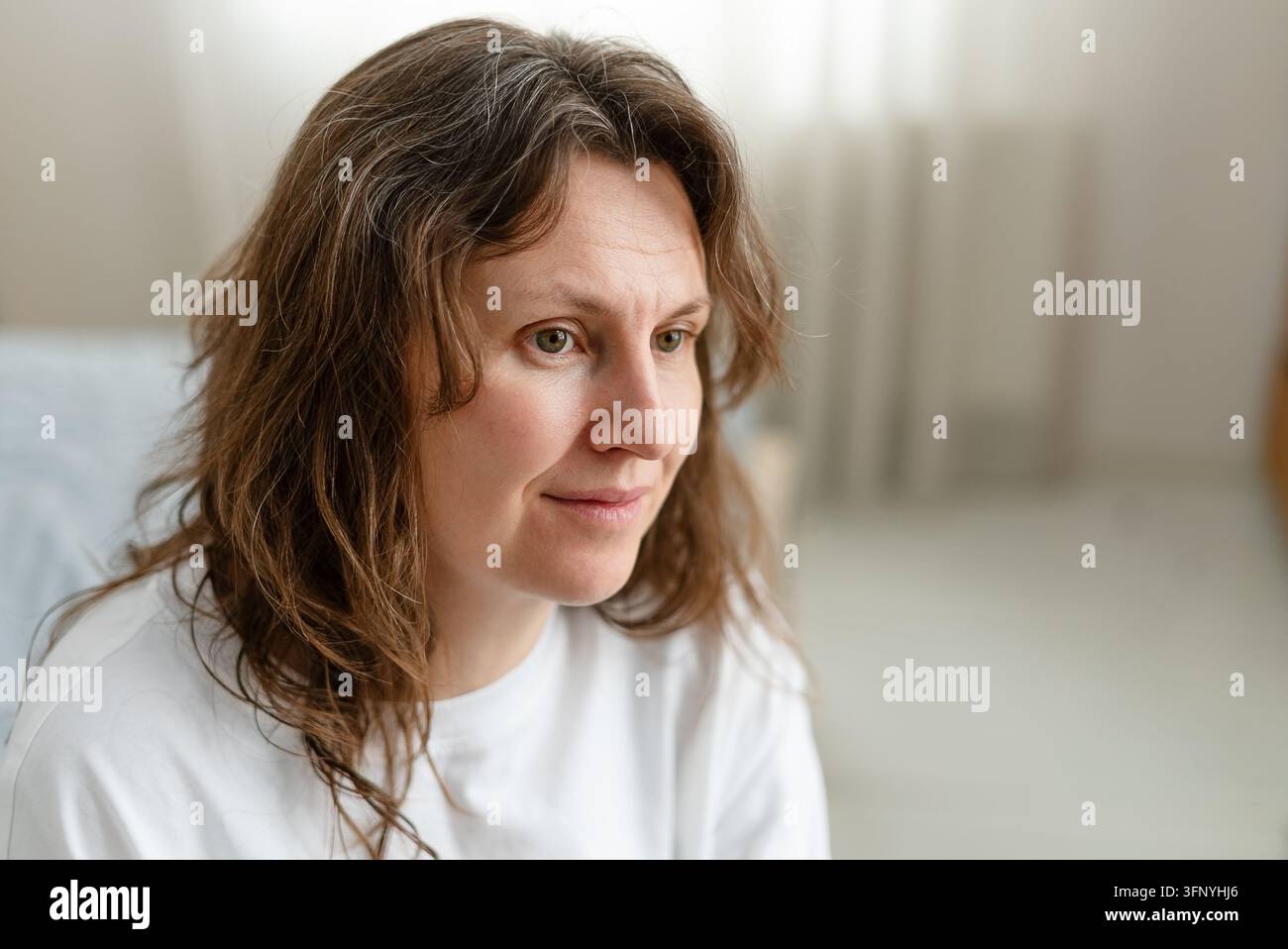 Une femme accepte pleinement ses cheveux grisonnants avec une expression de calme paisible. L'adulte mûre a fait la paix avec ce signe naturel du vieillissement. La mère embrasse ses mèches argentées comme faisant partie de son histoire. Banque D'Images