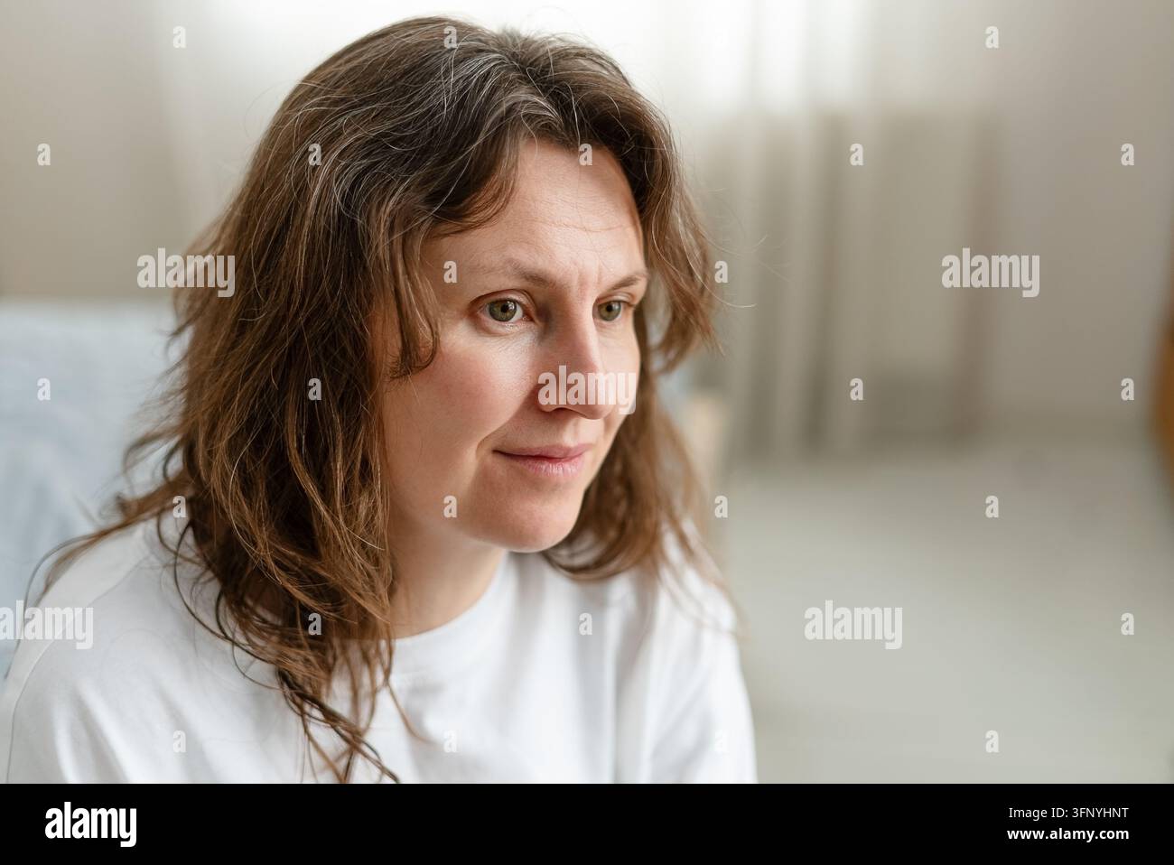 Une femme accepte pleinement ses cheveux grisonnants avec une expression de calme paisible. L'adulte mûre a fait la paix avec ce signe naturel du vieillissement. La mère embrasse ses mèches argentées comme faisant partie de son histoire. Banque D'Images