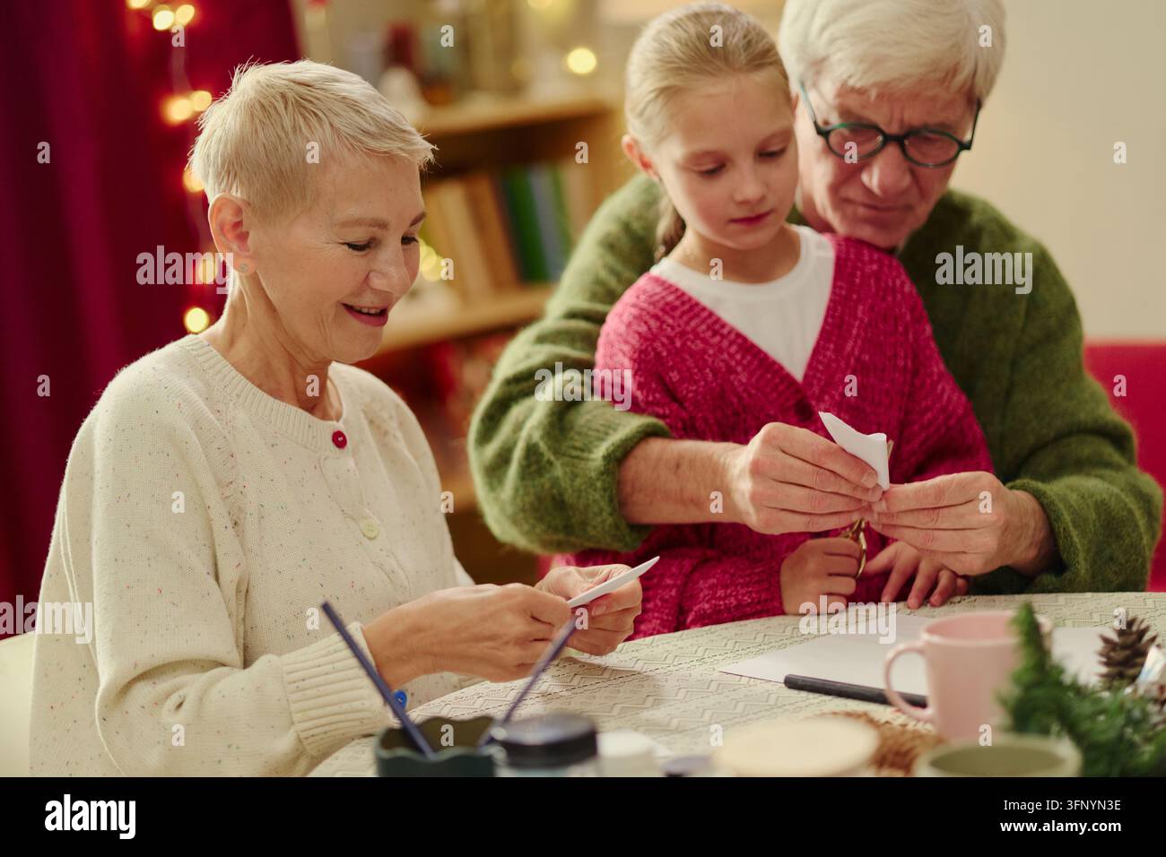 Couple de personnes âgées avec petite-fille faisant des loisirs créatifs en papier pour Noël Banque D'Images