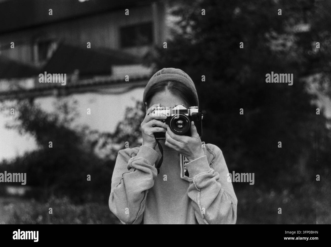 Jeune femme tenant un appareil photo vintage Zenit-E devant son visage en plein air. Banque D'Images