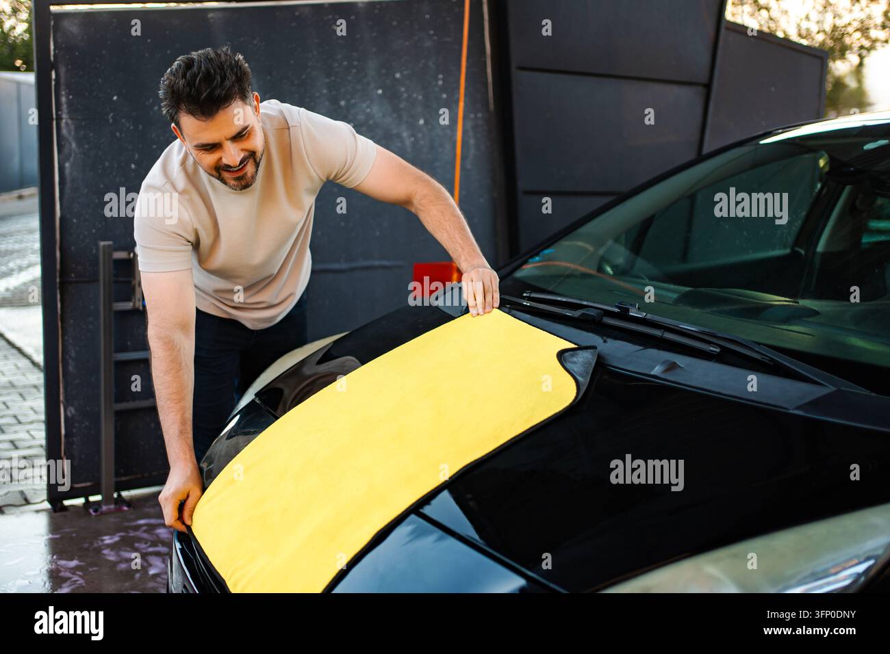 Homme essuyant une voiture noire avec un chiffon en microfibre Banque D'Images