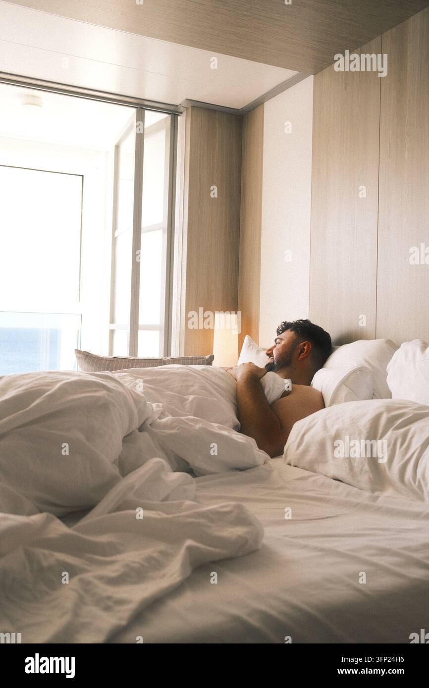 Homme allongé dans un lit d'hôtel lors d'une croisière de luxe Banque D'Images