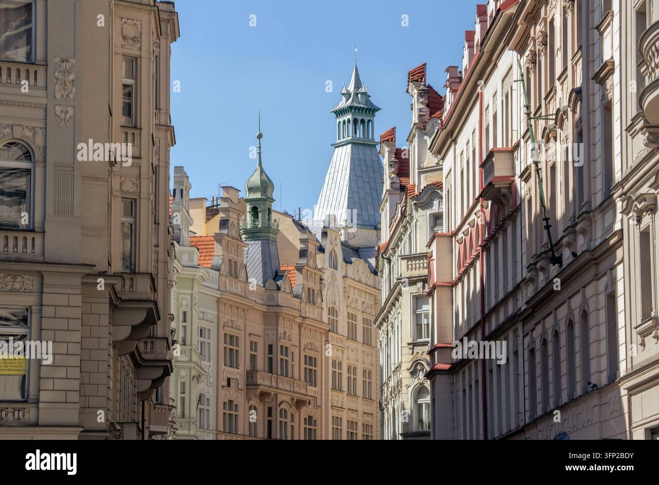 Une longue vue de rue à travers le centre de Prague montre des bâtiments historiques ornés, des toits en tuiles rouges et des tours distinctives créant une perspective urbaine en couches Banque D'Images