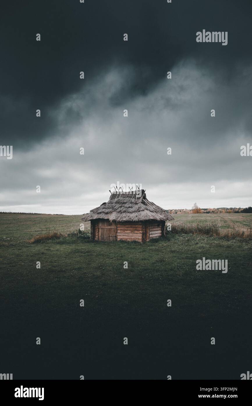 Vue de la cabane rustique Vale-Vargamae avec un toit de chaume traditionnel, située dans un vaste champ ouvert sous un ciel orageux sombre et dramatique à Vastse-Roosa, Vorse Banque D'Images