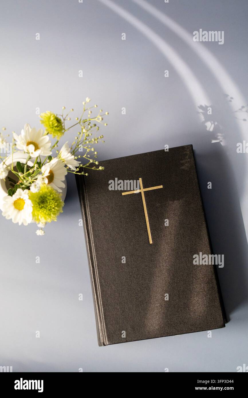 Sainte Bible avec croix dorée et fleurs au soleil, fond de foi chrétienne Banque D'Images