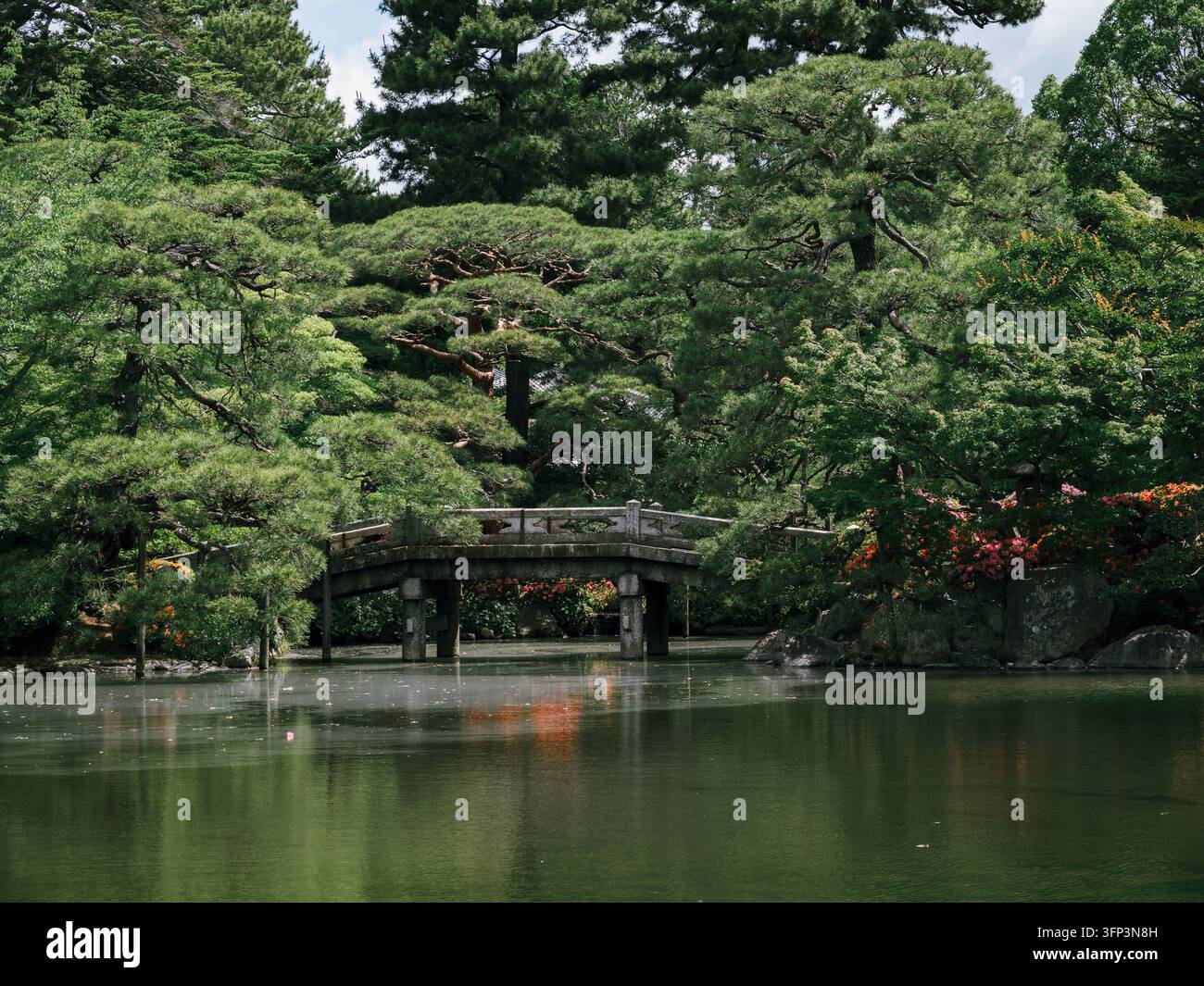 Pont de pierre sur un étang parmi les pins et les azalées en fleurs dans le jardin du Palais impérial de Kyoto, Kyoto, Japon Banque D'Images