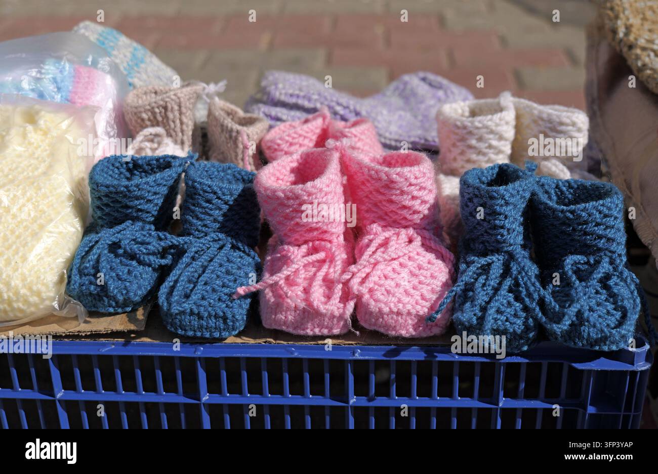Des chaussons tricotés à la main colorés sont soigneusement disposés sur une caisse en plastique bleue, mettant en valeur l’artisanat local et offrant une douce chaleur pour les nourrissons Banque D'Images
