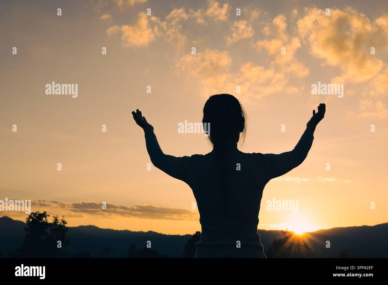 Une silhouette d'une femme debout sur un sommet montagneux avec les bras grands ouverts, embrassant le lever du soleil matinal, symbolisant la liberté, l'adoration. Banque D'Images