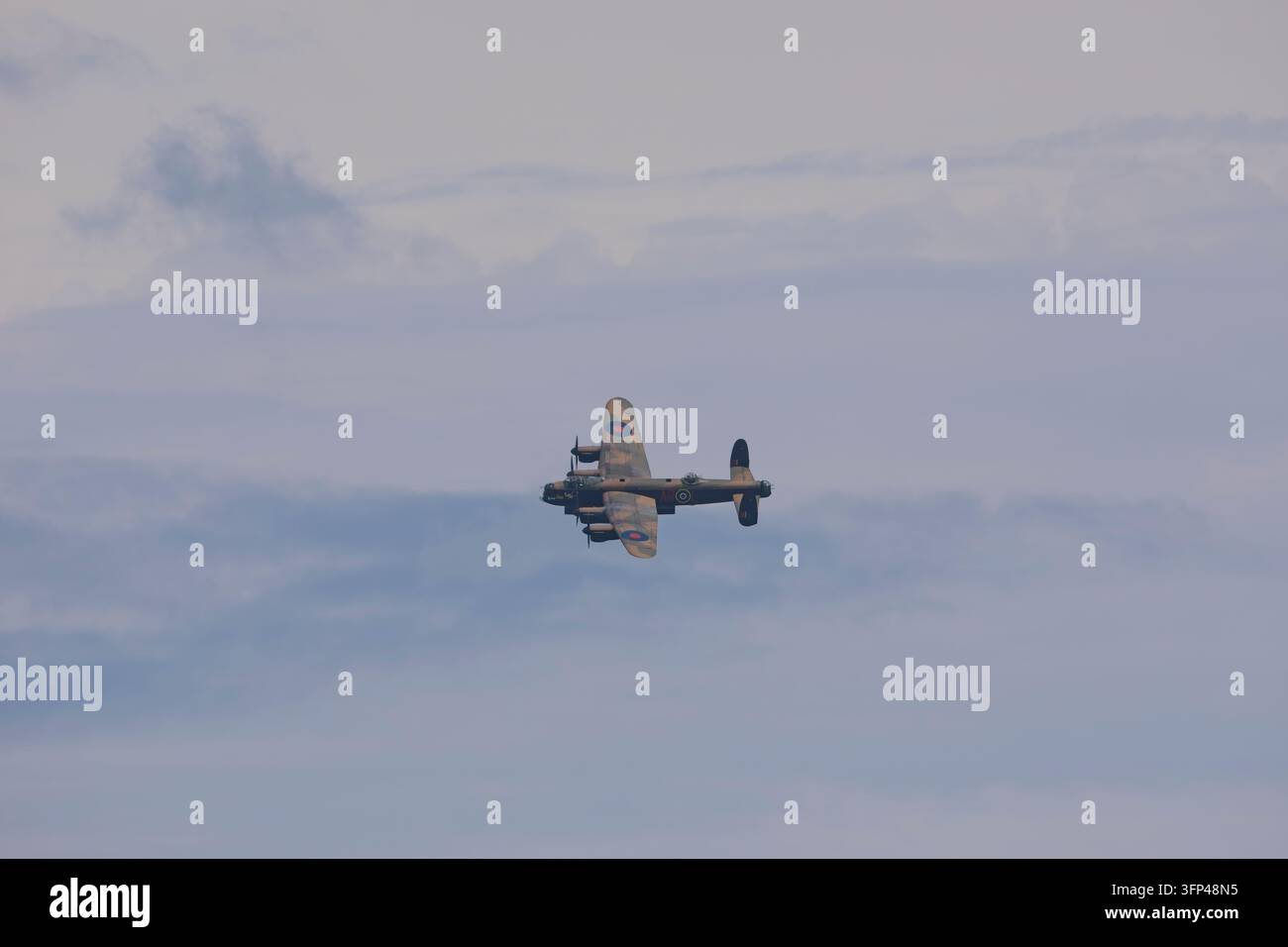 Vue lointaine d'un bombardier lourd historique Avro Lancaster virant à travers des nuages épars et un ciel bleu clair lors d'une démonstration aérienne. Banque D'Images