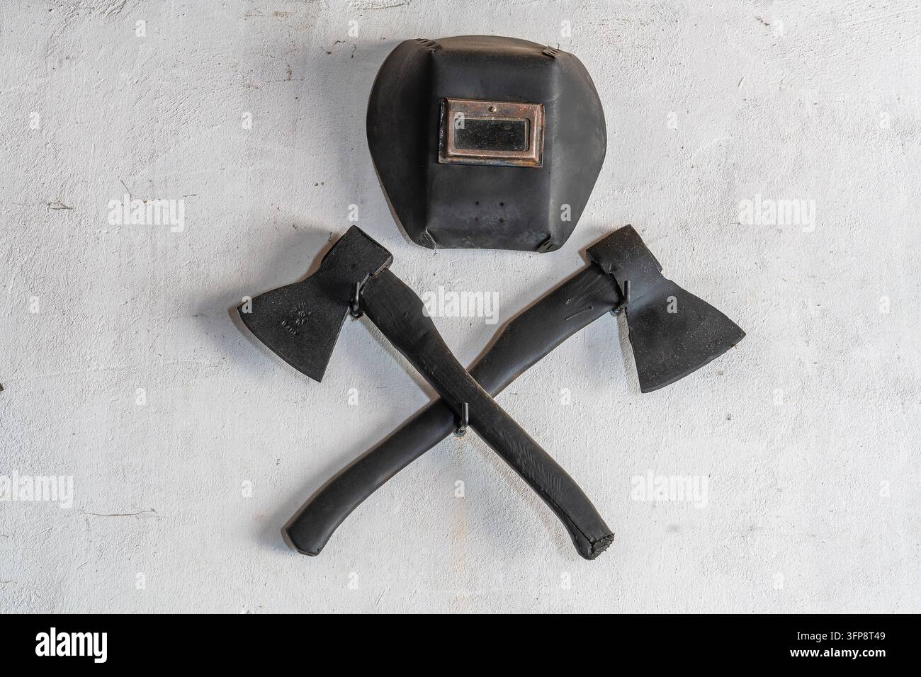 Deux haches noires croisées et un masque de protection pour le soudage sur un mur de stuc blanc, gros plan Banque D'Images