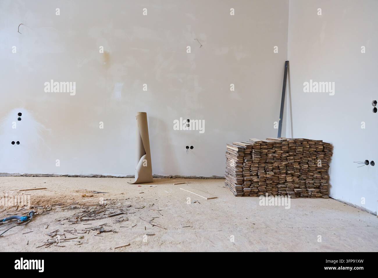 Un appartement en rénovation présente des planches de parquet empilées prêtes à être posées, avec des murs exposés et des prises électriques visibles. Banque D'Images