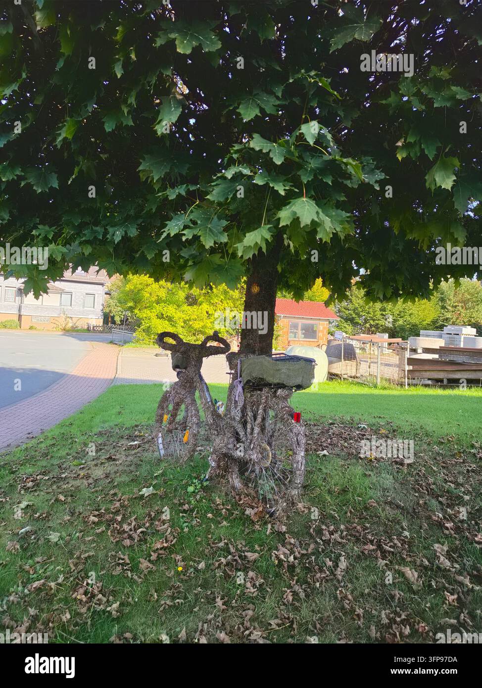 Un vieux vélo vintage artistiquement décoré de feuillage vert luxuriant et de fleurs, garé contre un tronc d'arbre dans une ville allemande - Image de stock capturée avec un smartphone