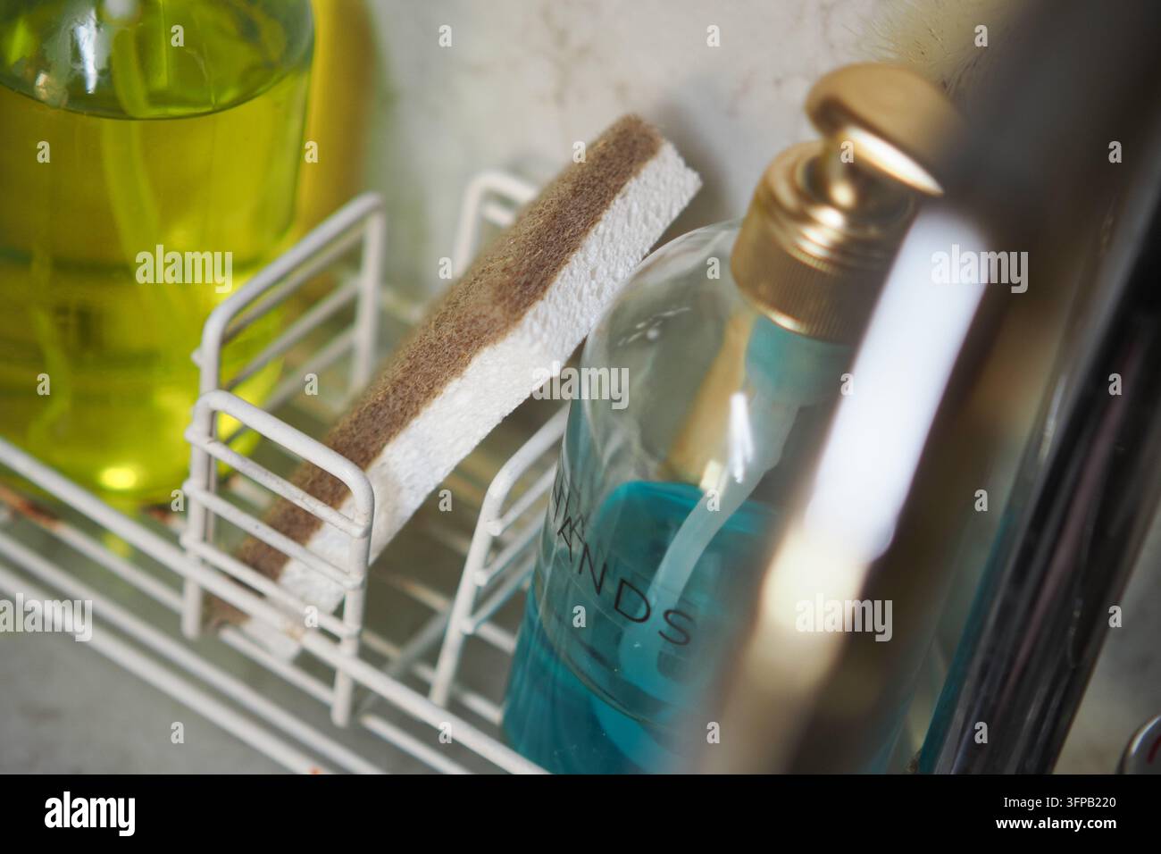 Produits de nettoyage sur une étagère dans une cuisine avec diverses bouteilles et une éponge Banque D'Images